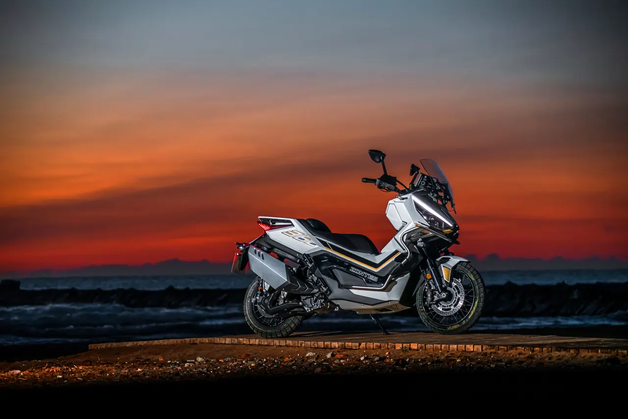 Zontes 368G ADV blanca estacionada frente al mar con un atardecer rojizo